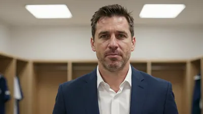 A head-and-shoulders portrait of a 40-45 year old male football coach, wearing a navy blue blazer over a white dress...