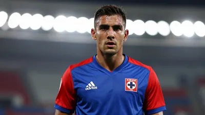 Mid-30s muscular defender, waist-up, intense gaze, wearing Cruz Azul home jersey - blue base with red sleeves, crisp...