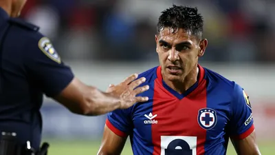 Mid-30s muscular Cruz Azul forward, intense gaze, waist-up, wearing the blue-red home jersey with the crest on the left...
