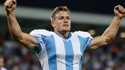 A tight action shot of a muscular, anonymous 25-30 year old male footballer in a blue and white striped jersey...