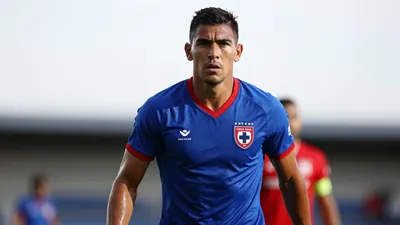 Mid-30s muscular forward, waist-up, wearing Cruz Azul home kit - blue shirt with red trim, crisp club crest on left...
