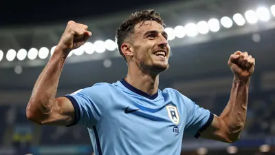 A tight action shot of a midfielder in a light blue jersey celebrating a goal in a stadium