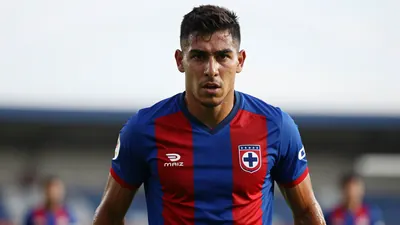 A mid-30s anonymous Cruz Azul forward, muscular, waist-up, intense expression, eyes fixed on the camera, wearing the...
