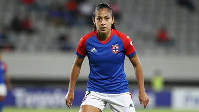 Mid-shot of a 22-year-old female forward, athletic build, dark hair pulled back, eyes focused, wearing Cruz Azul home kit...