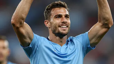 A photorealistic shot of a muscular male footballer in his mid-20s, wearing a sky blue jersey with smooth fabric...