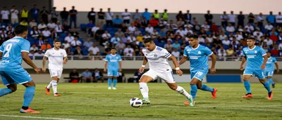 A tense moment on a sun-lit stadium pitch, two anonymous players locked in a duel: one in plain sky-blue shirt and...