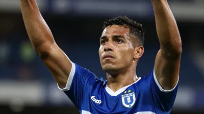A Cruz Azul player in a blue jersey with white trim, celebrating a goal with arms raised