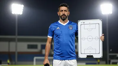 A 35-year-old, 5'10" tall, athletic-looking, dark-haired, and bearded assistant coach of Xolos, wearing a blue jersey and...