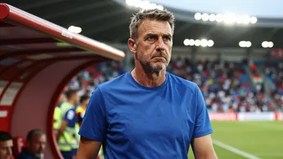 A tight action crop of a blue-shirted coach in his mid-40s, with a stern expression, standing in the tunnel of a stadium...