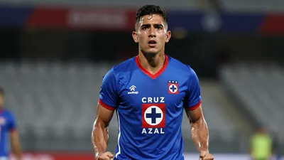 Mid-shot of a determined 24-year-old forward, muscular build, wearing Cruz Azul home kit - blue shirt with red trim...