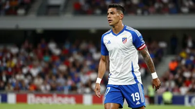 A photorealistic image of a Deportivo player, likely Luismi Cruz, in a floodlit stadium, wearing a white jersey with blue...